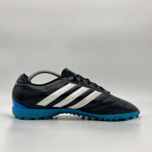 A side profile view of a black Adidas Goletto V TF turf soccer shoe with white stripes and a blue outsole.
