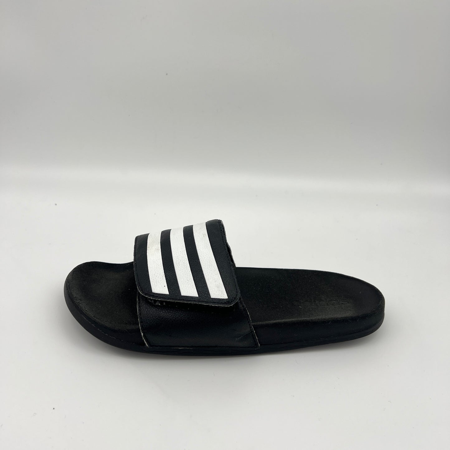 Side profile of black Adidas Adilette Comfort slides with an adjustable three-stripe strap and cushioned footbed.