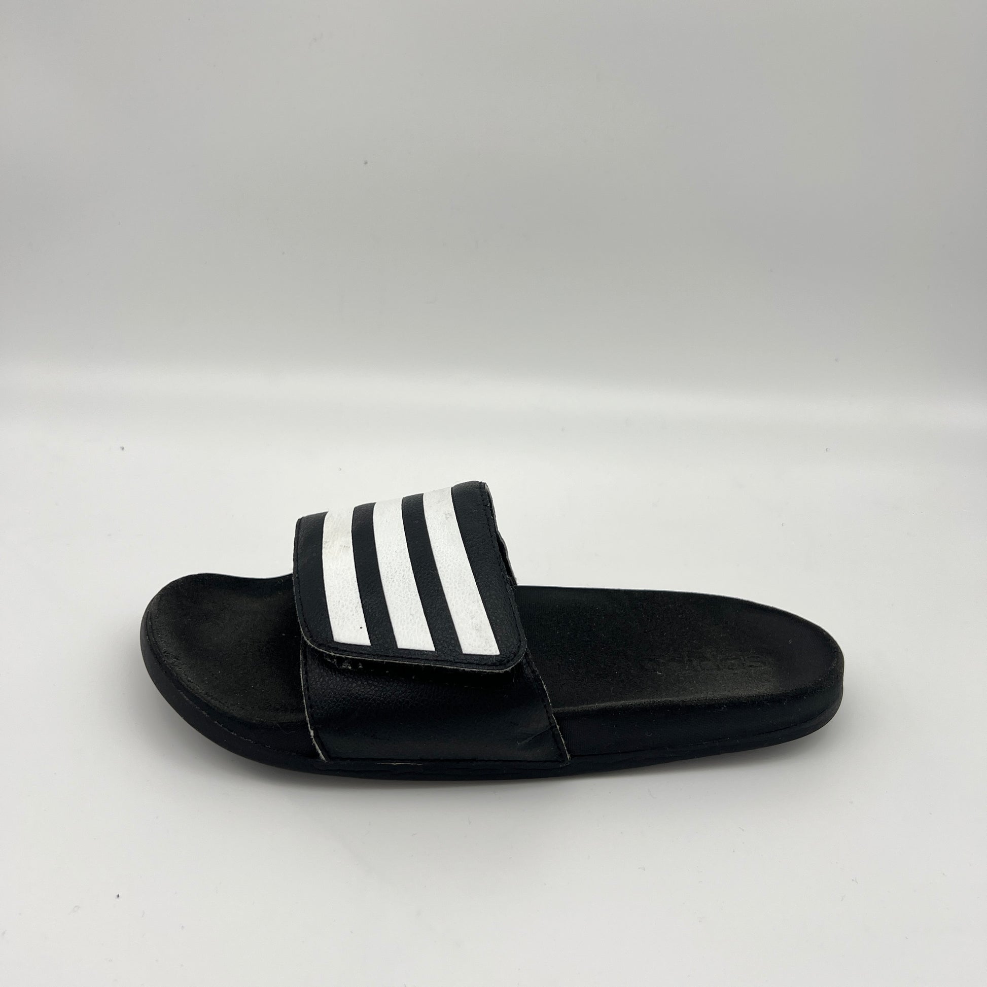 Side profile of black Adidas Adilette Comfort slides with an adjustable three-stripe strap and cushioned footbed.
