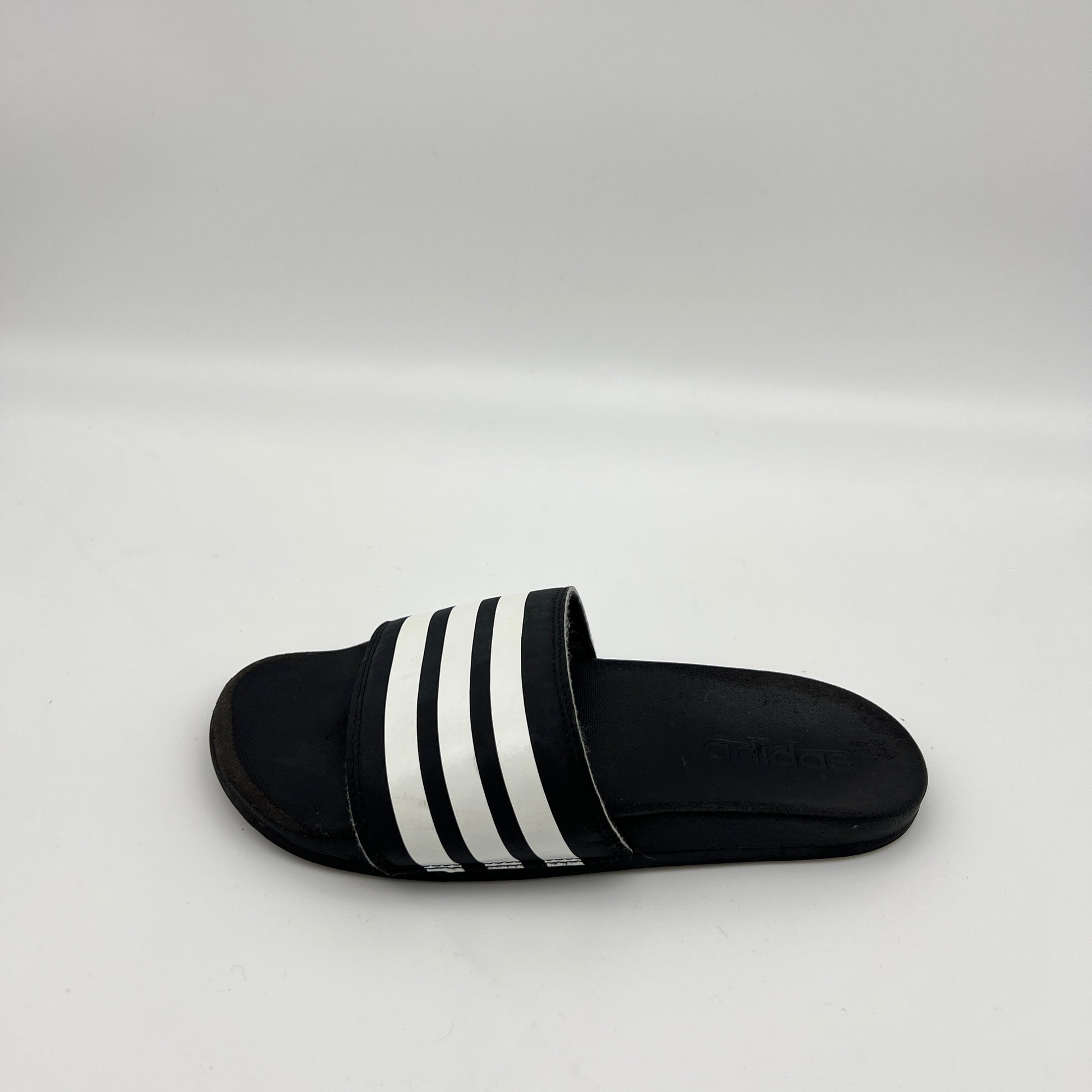 Single black Adidas Adilette Comfort slide with three white stripes on a white background.