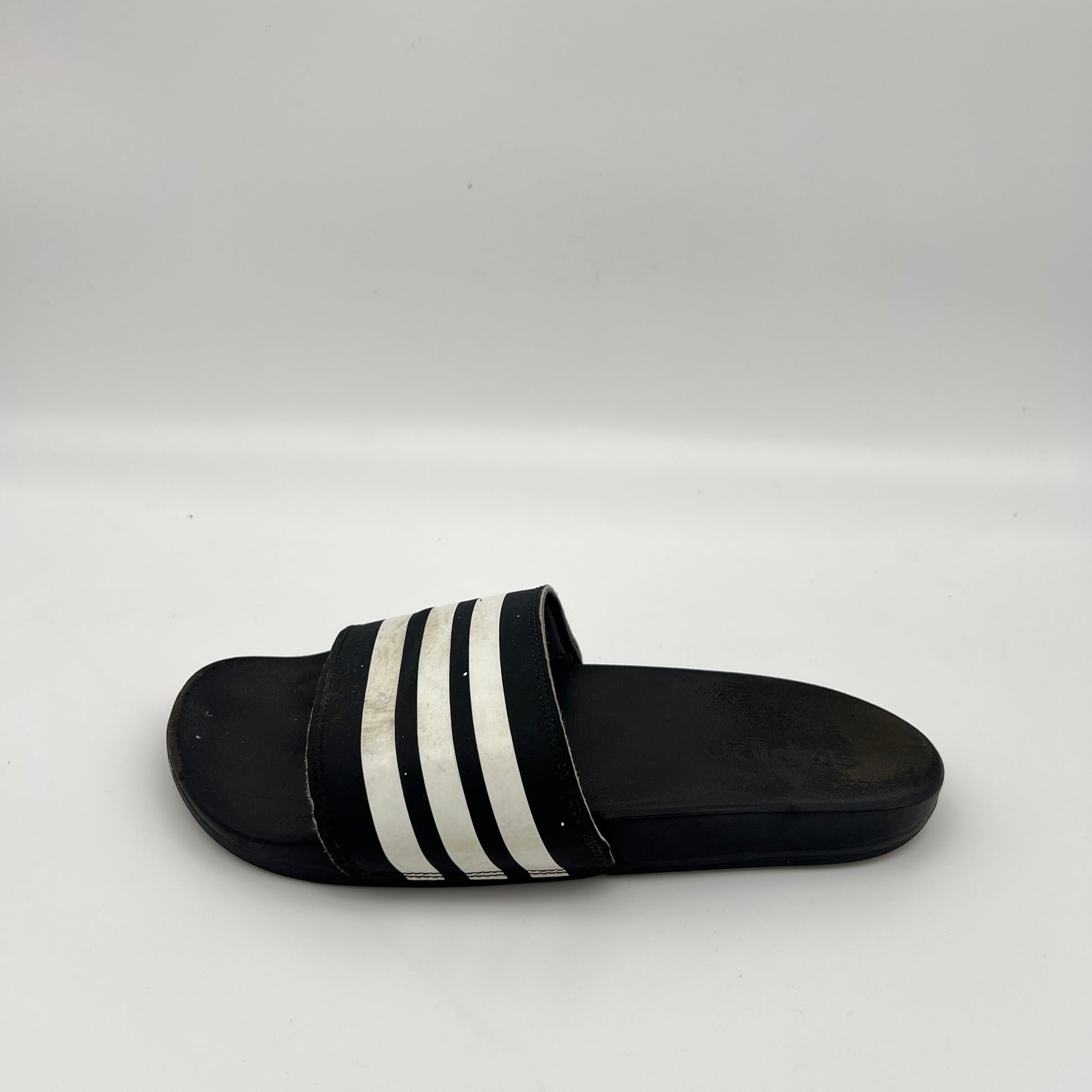 A single black Adidas Adilette Comfort slide sandal with three white stripes on a light grey background.