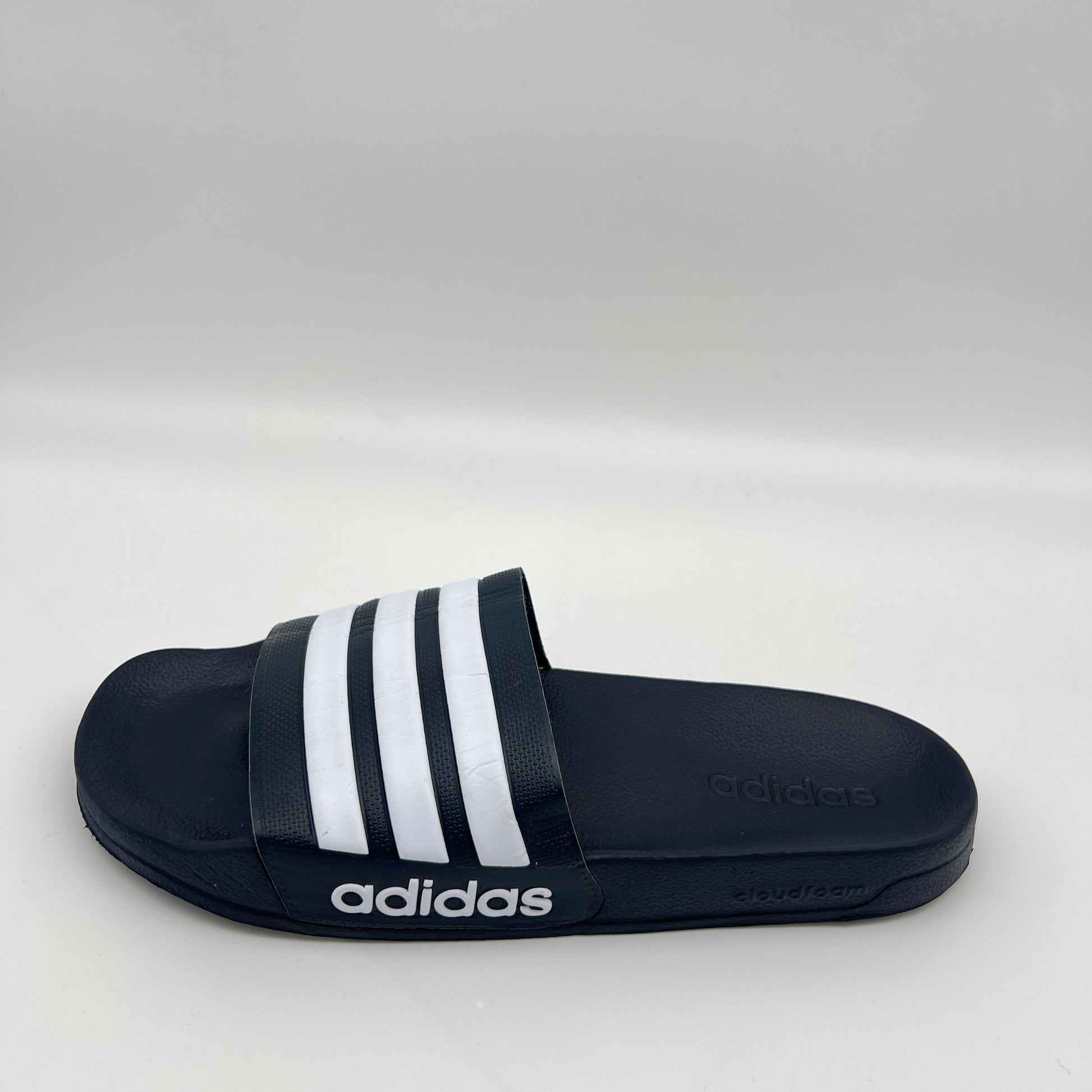 Black Adidas slide sandal with white stripes on a light gray background