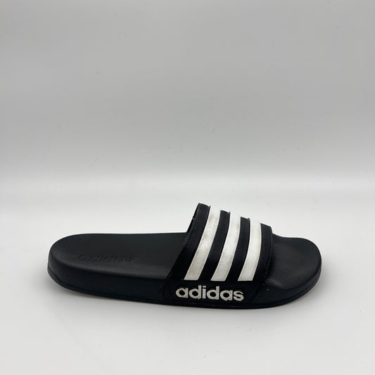 Side profile of a black Adidas Adilette Shower slide with three white stripes on the strap and a white Adidas logo on the black sole against a white background.