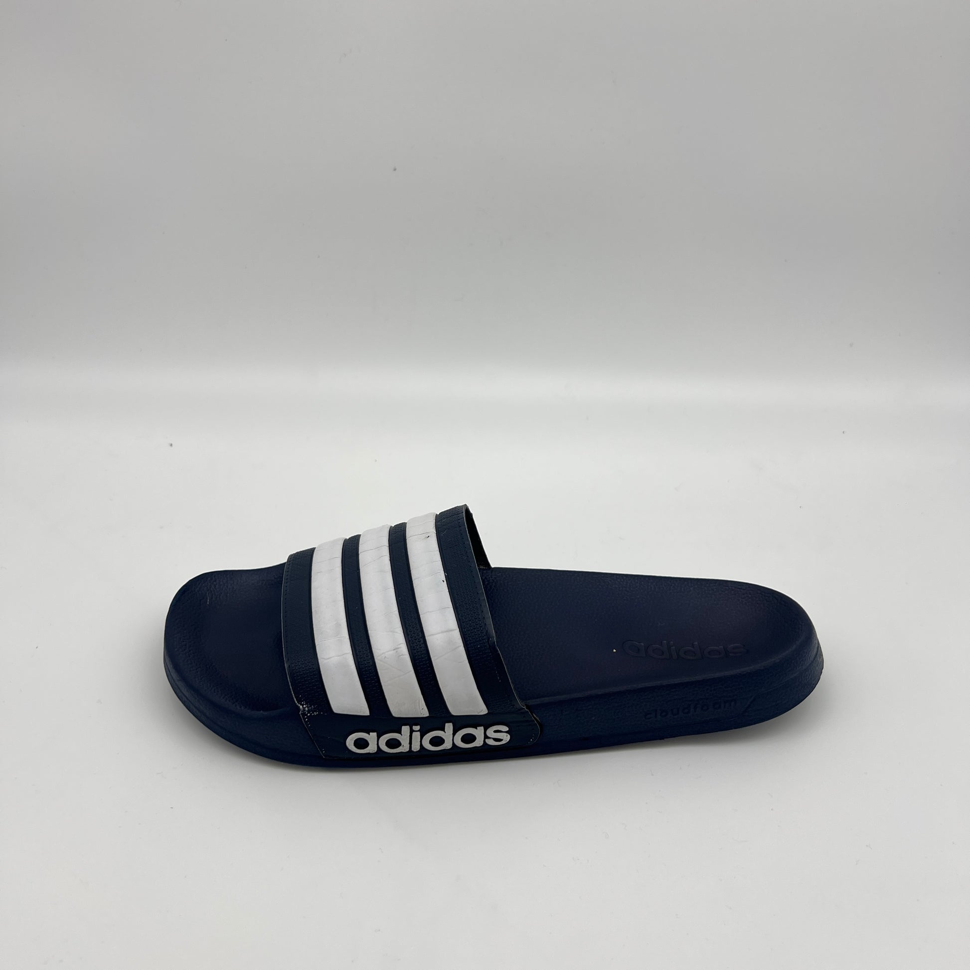 Side profile of navy blue Adidas Adilette Shower slides with white three-stripes and Cloudfoam logo.