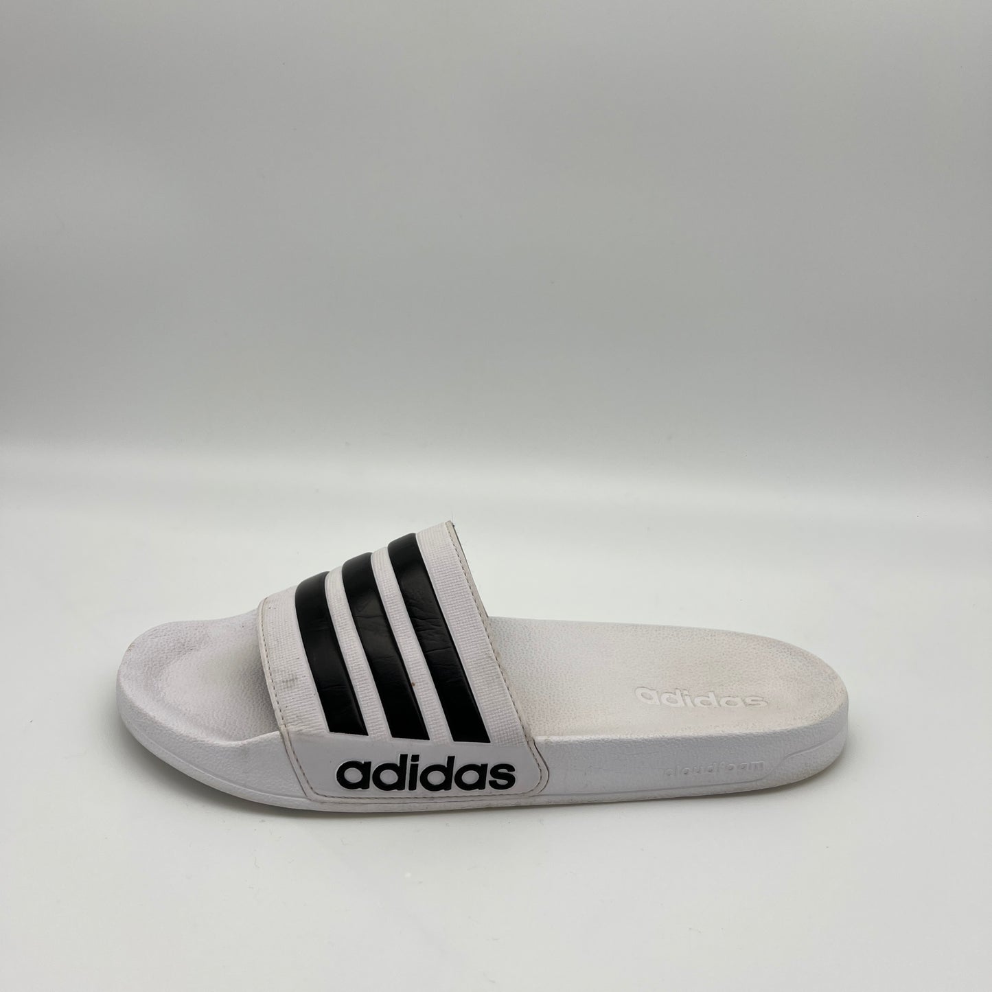 Gray Adidas slide sandal with black stripes on a light gray background
