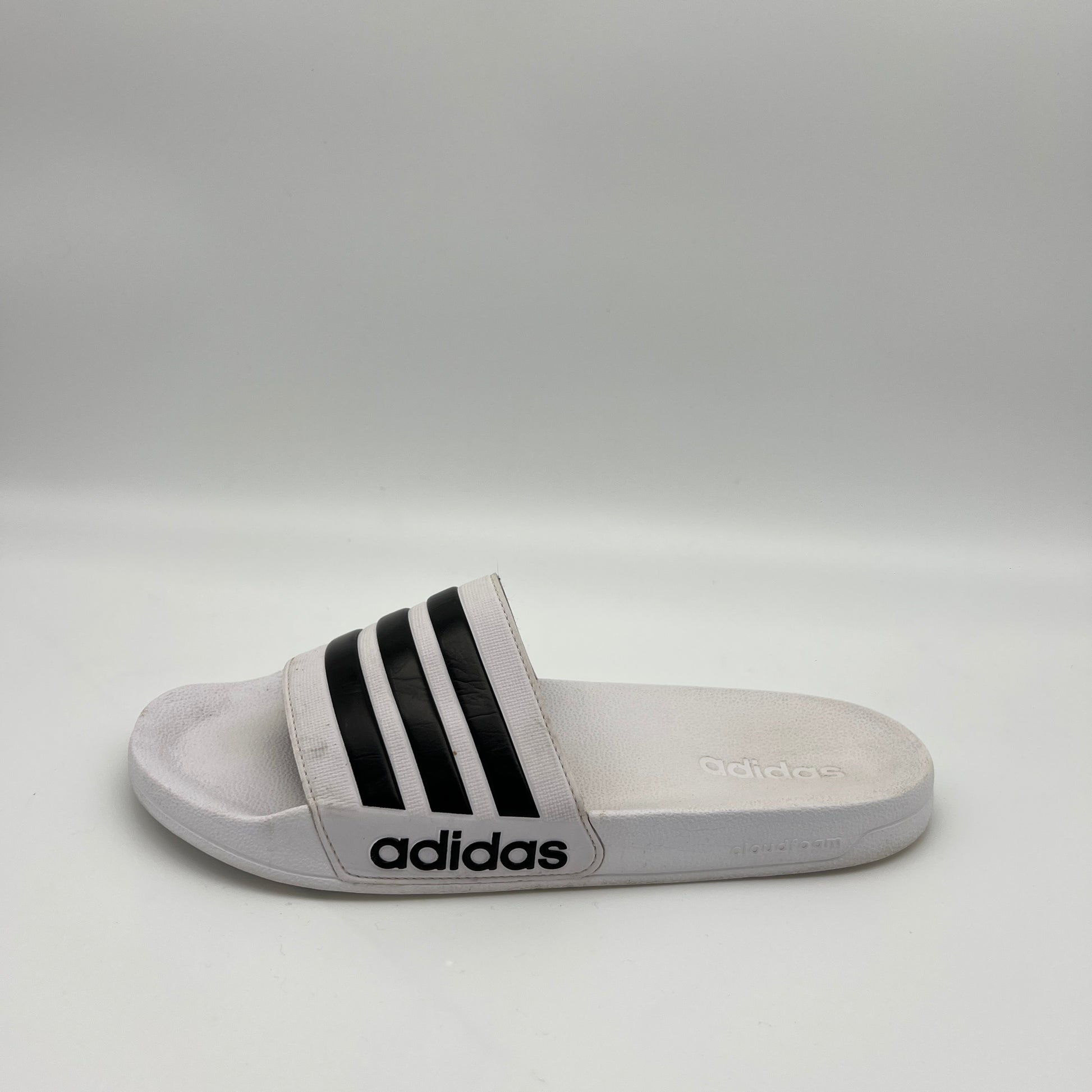 Gray Adidas slide sandal with black stripes on a light gray background