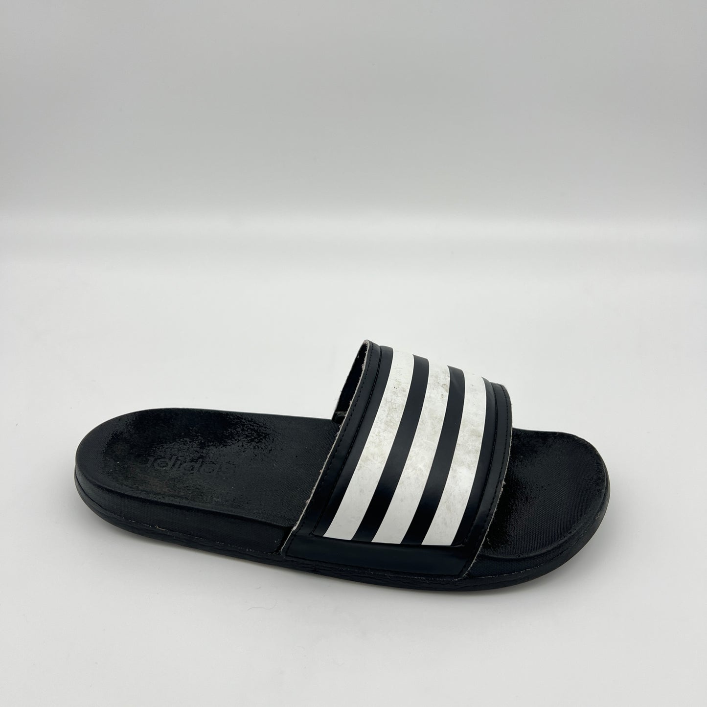 Black slide sandal with white stripes on a light gray background