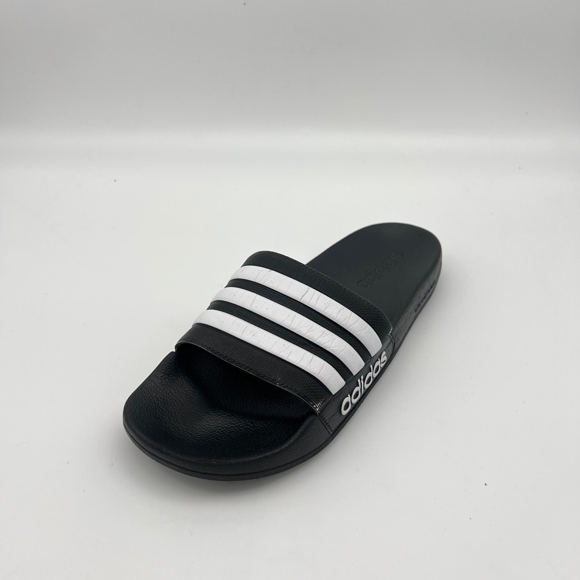 Side view of a black Adidas Adilette Shower slide featuring white three-stripes and a Cloudfoam sole