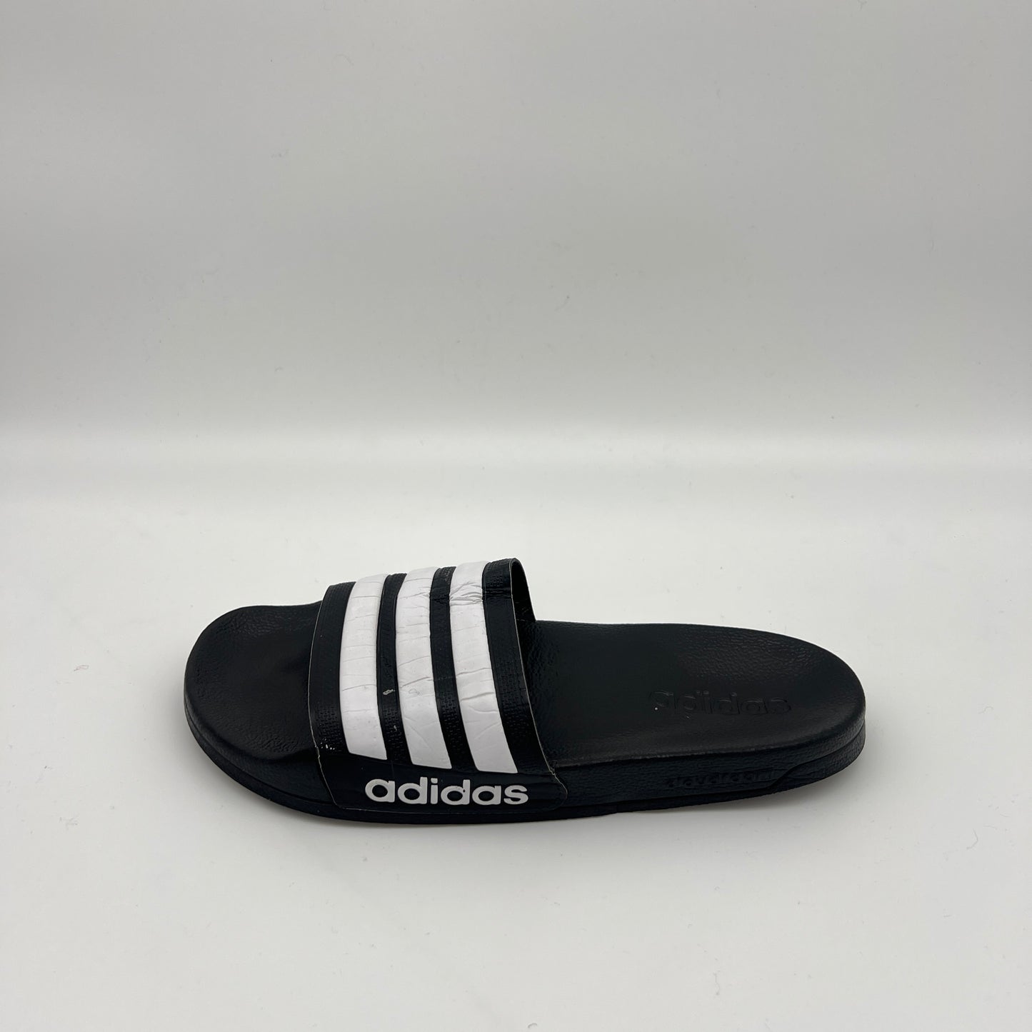 Side view of black Adidas Adilette Shower Slides with white stripes on the strap and a white Adidas logo on the side of the Cloudfoam midsole.
