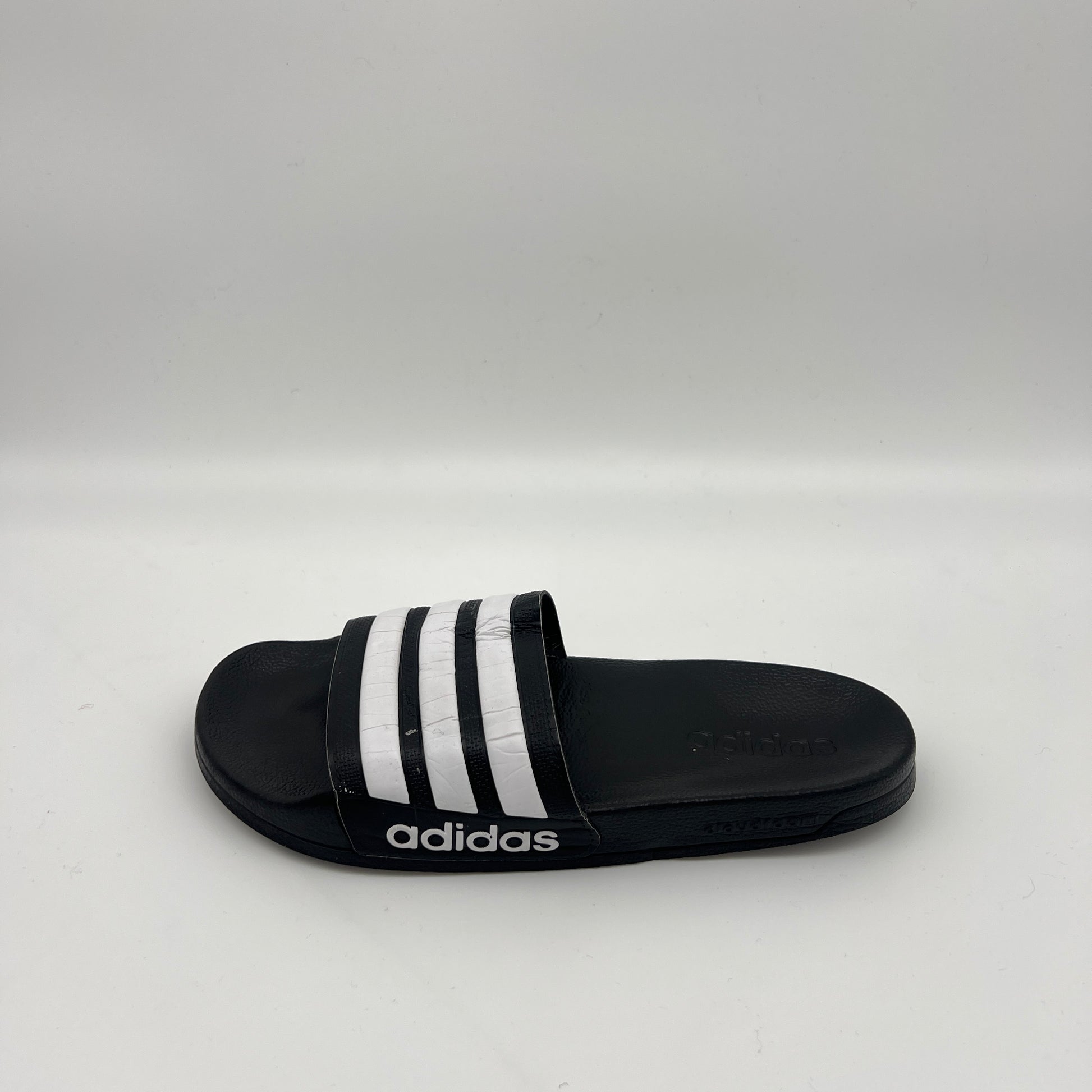 Side view of black Adidas Adilette Shower Slides with white stripes on the strap and a white Adidas logo on the side of the Cloudfoam midsole.