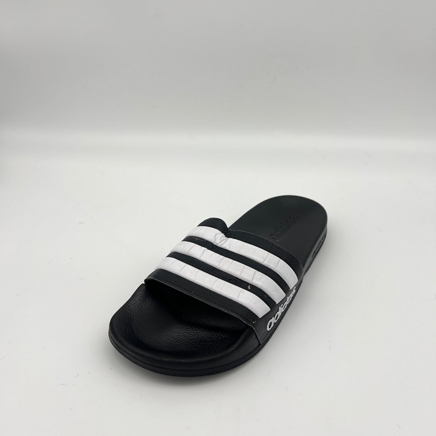 Black slide sandal with white stripes on a light gray background