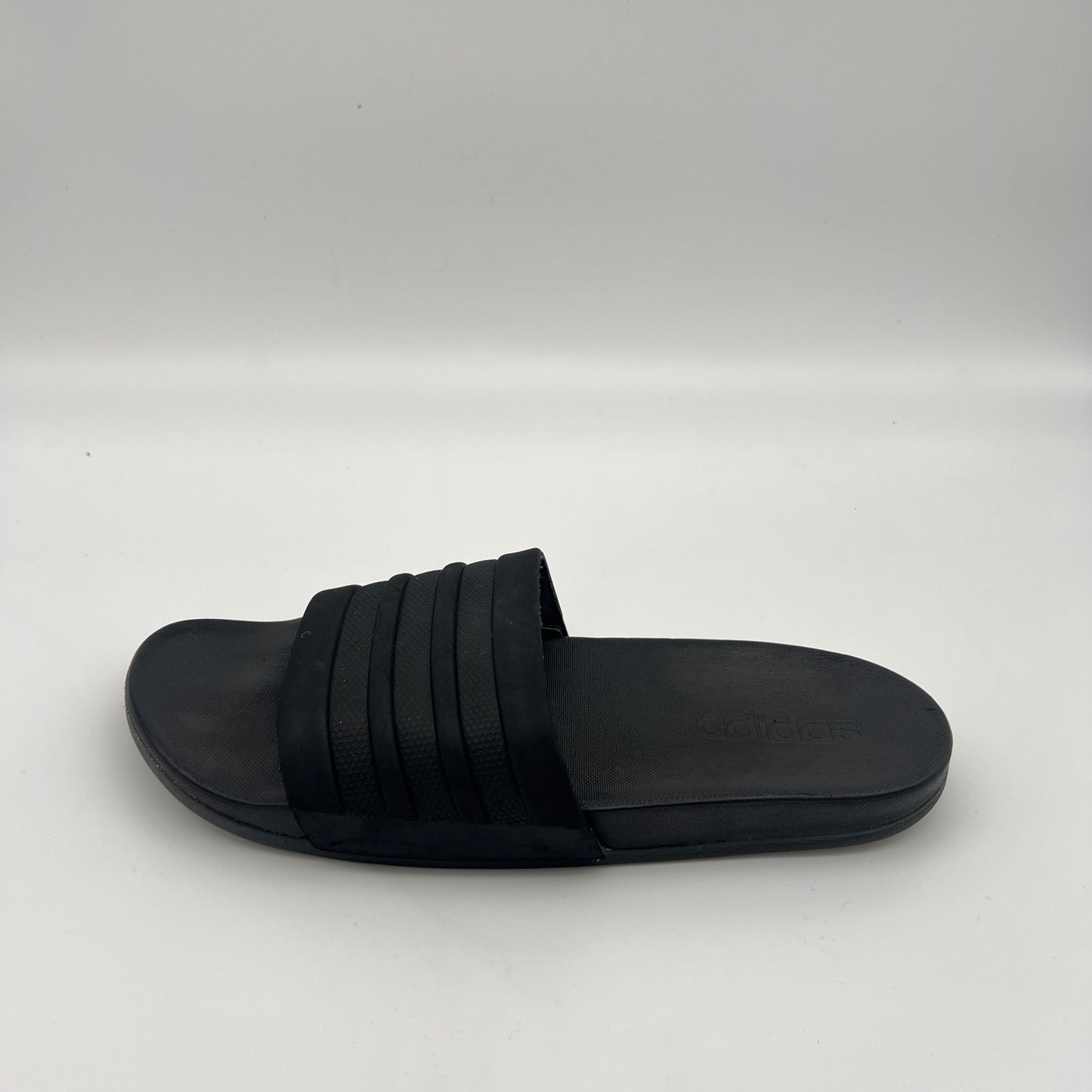 All-black Adidas Adilette Shower slides with tonal three-stripes and a contoured footbed.