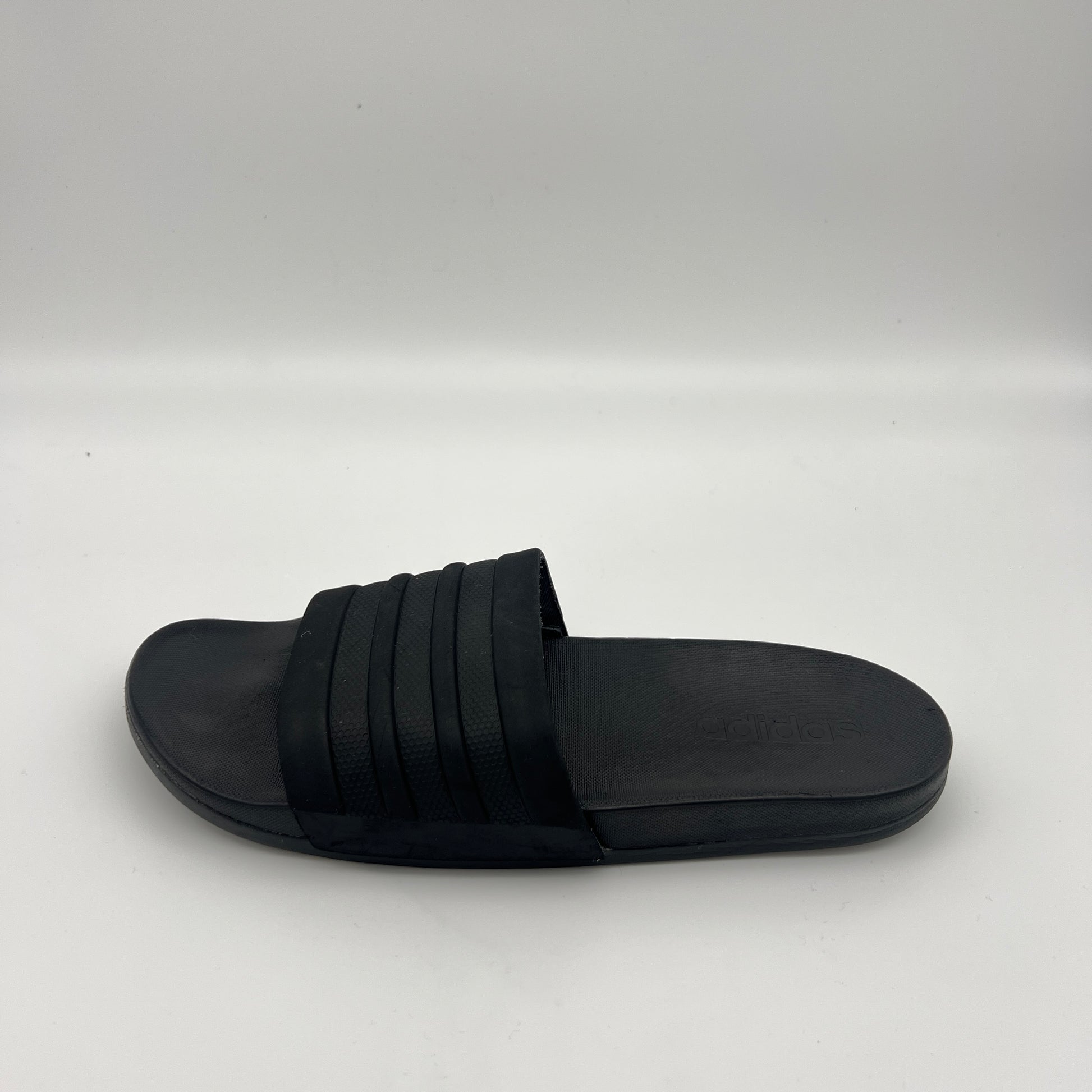All-black Adidas Adilette Shower slides with tonal three-stripes and a contoured footbed.