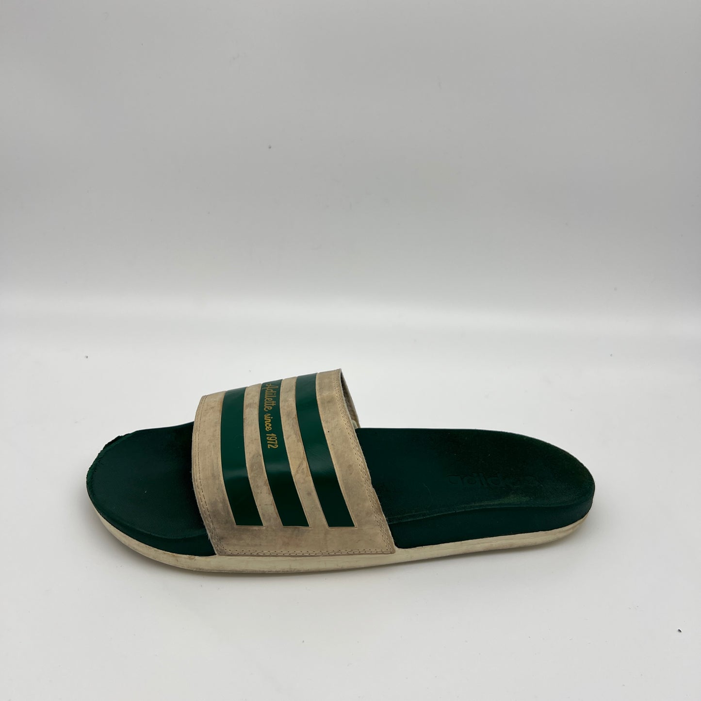Adidas Adilette Since 1972 slides in off-white and forest green.