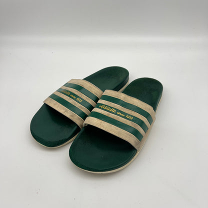Side view of retro Adidas Adilette sandals with green 3-Stripes and gold-foil "Since 1972" lettering on an off-white strap.