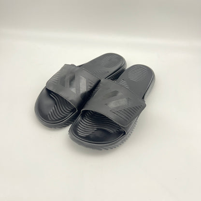 A side profile of an all-black Adidas Alphabounce slide featuring an adjustable strap with debossed branding and a thick, contoured Bounce cushioned sole.