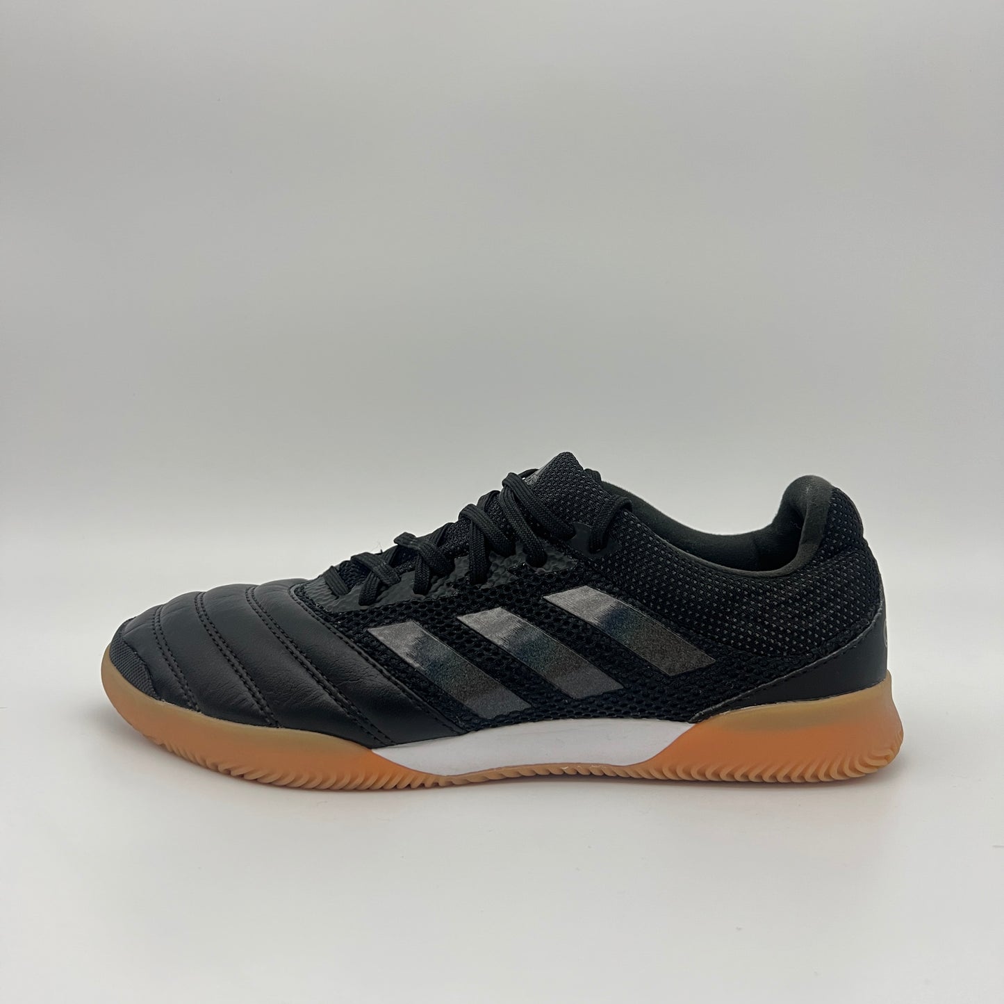 Side view of a black Adidas Copa 19.3 indoor soccer shoe with tonal three stripes, a white midsole, and a tan gum sole on a gray background.