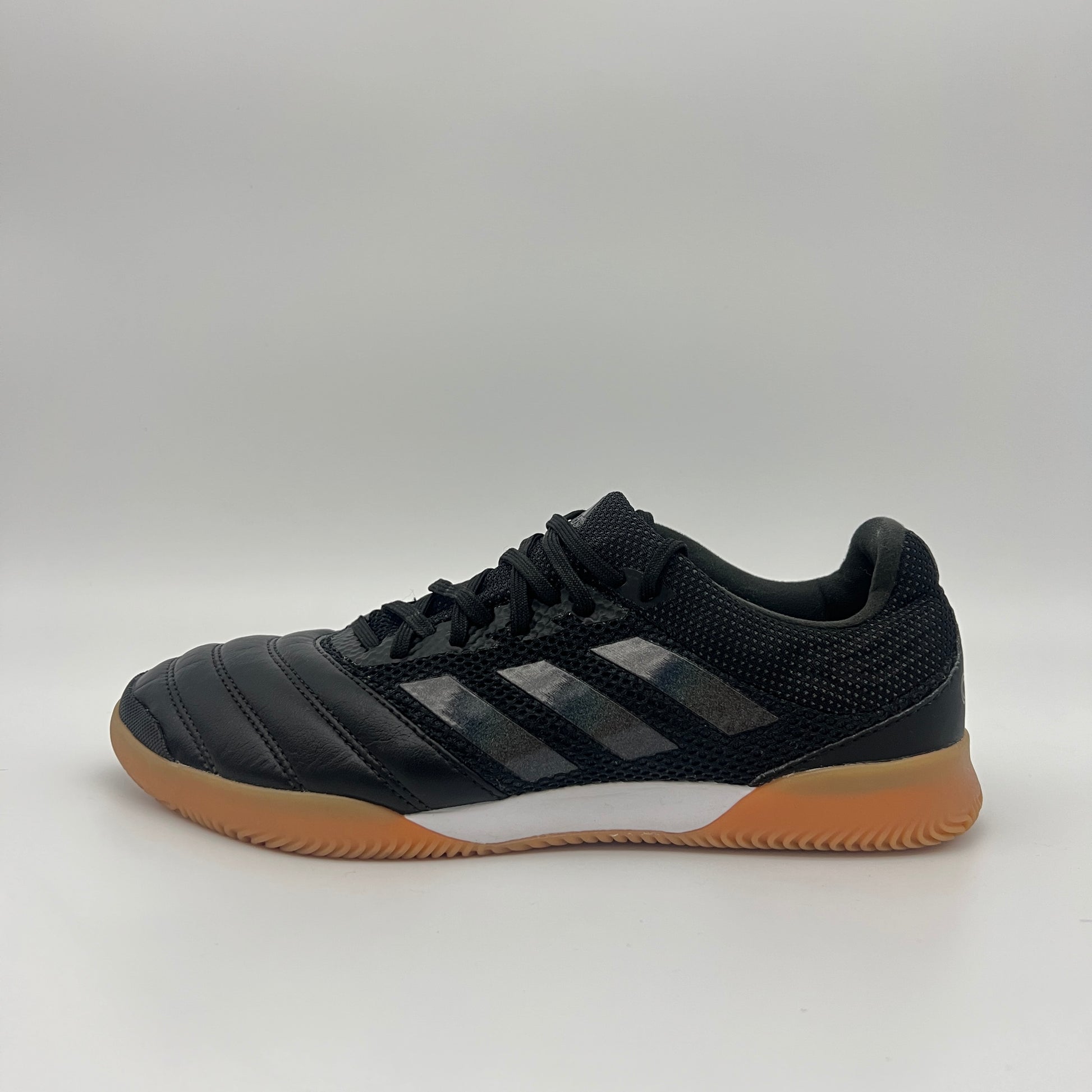 Side view of a black Adidas Copa 19.3 indoor soccer shoe with tonal three stripes, a white midsole, and a tan gum sole on a gray background.
