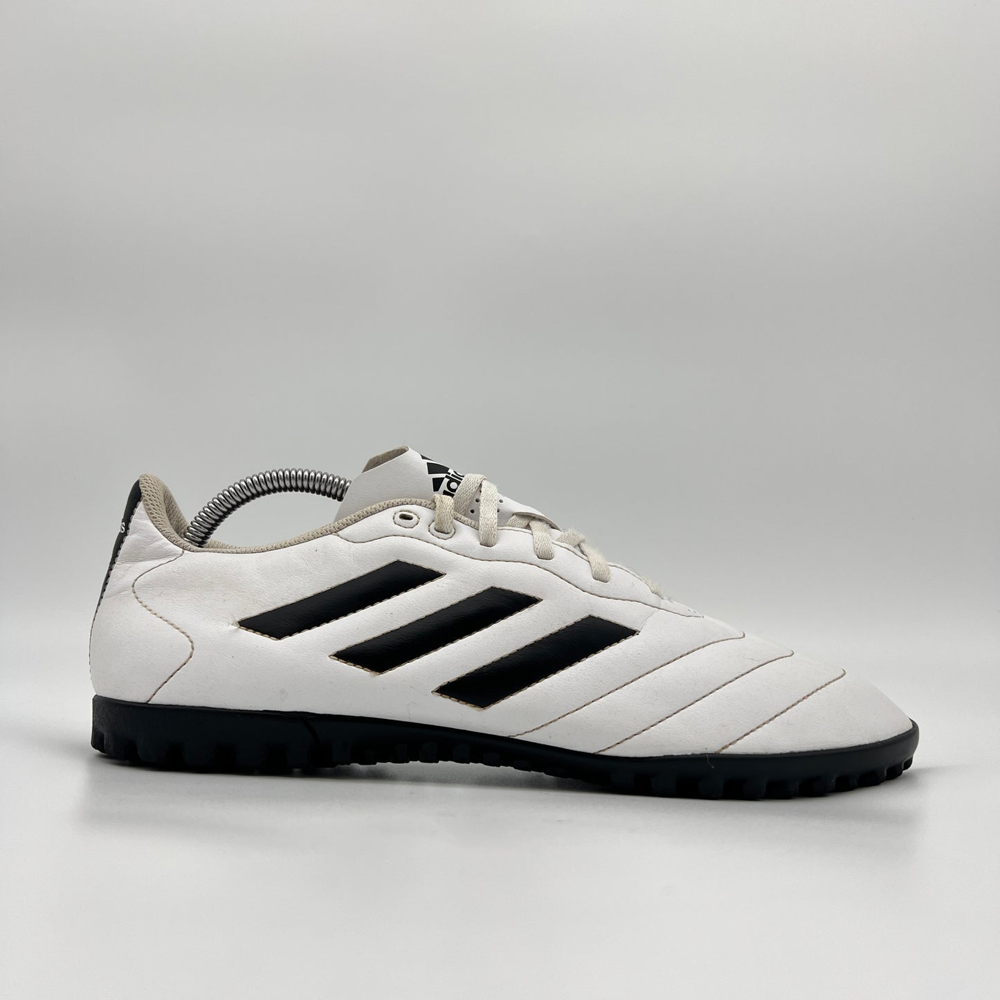 A side profile view of a white Adidas Goletto VIII TF turf soccer shoe with black stripes and a black outsole.