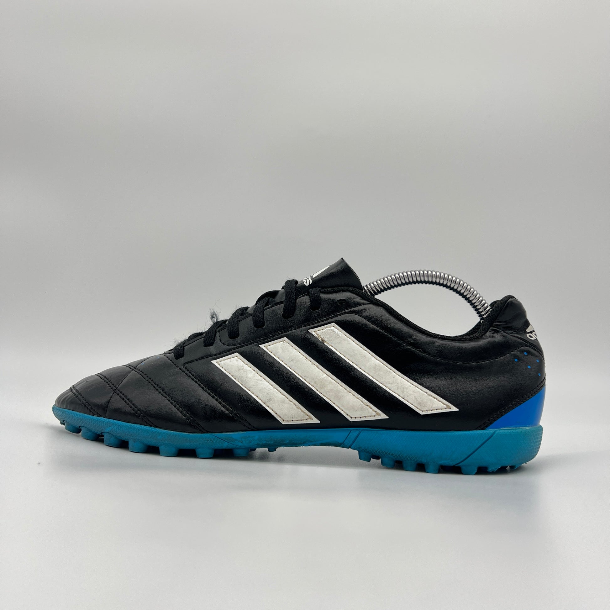 A side profile view of a black Adidas Goletto V TF turf soccer shoe with white stripes and a blue outsole.