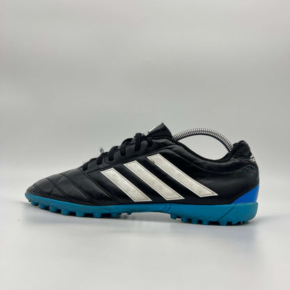 A side profile view of a black Adidas Goletto V TF turf soccer shoe with white stripes and a blue outsole.