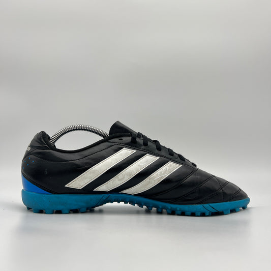 A side profile view of a black Adidas Goletto V TF turf soccer shoe with white stripes and a blue outsole.