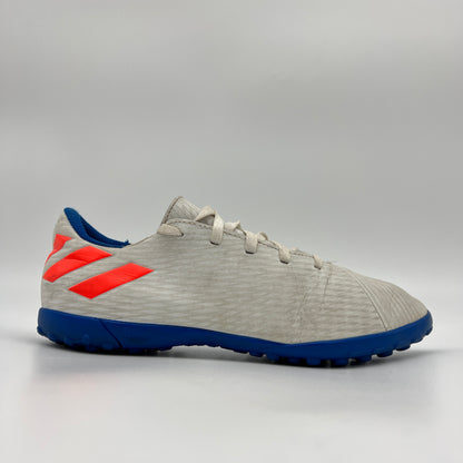 A side profile view of an Adidas Nemeziz Messi 19.4 TF turf soccer shoe in white with red stripes and a blue outsole.