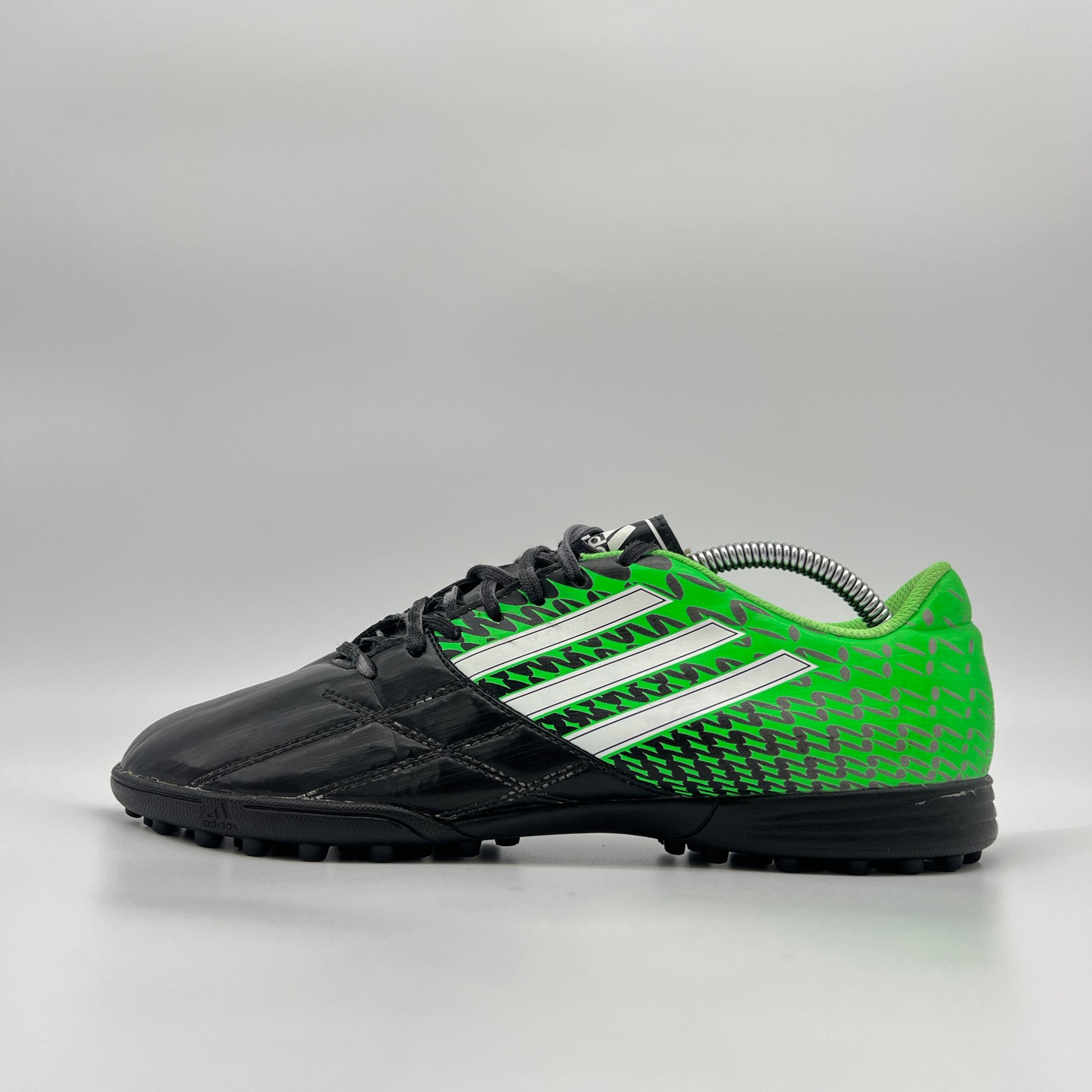 Side profile of a black and neon green Adidas Neoride TRX TF soccer shoe, featuring white stripes and a multi-studded turf outsole