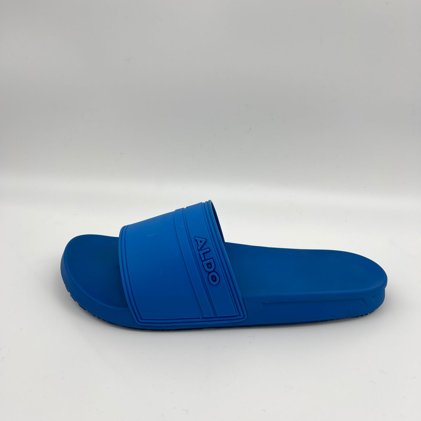 A side view of a solid blue Aldo Dinmore slide sandal featuring a thick rubber strap with a debossed Aldo logo on a contoured footbed.