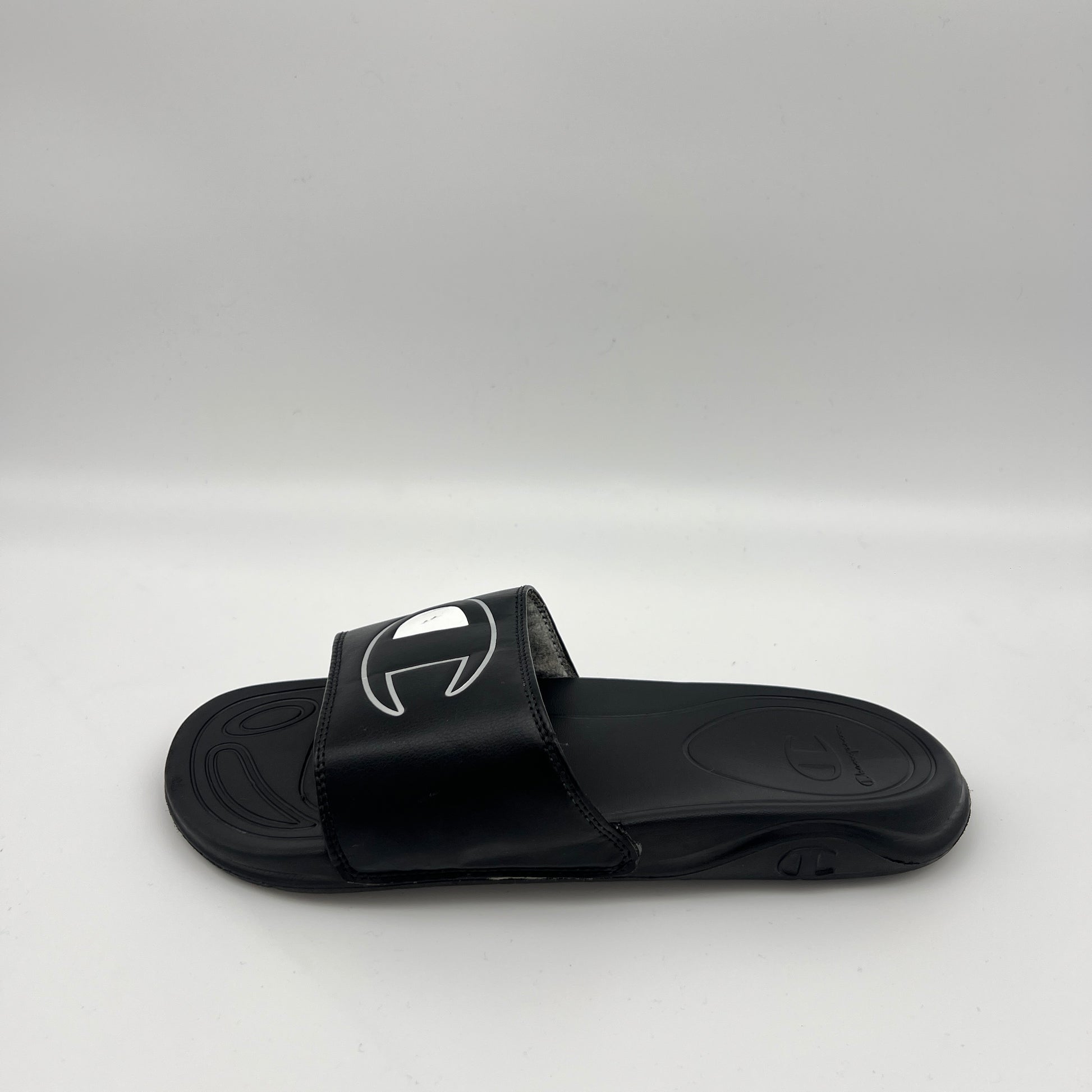 Pair of black Champion IPO Squish slide sandals featuring a raised white oversized "C" logo on the strap against a clean white background.
