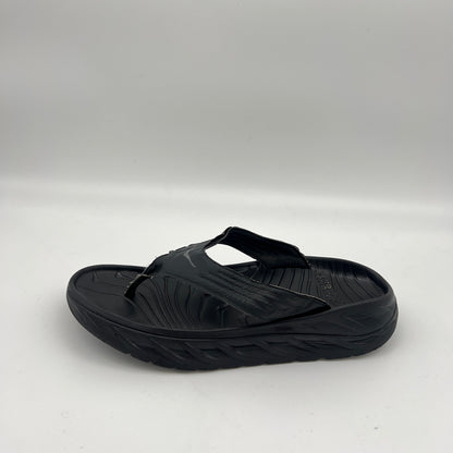 Side view of a black Hoka One One Ora Recovery Flip sandal with a thick cushioned midsole and textured footbed on a white background