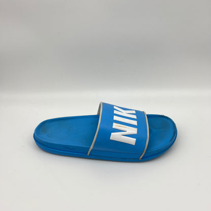 Side view of a bright blue Nike Benassi JDI slide featuring a wide blue strap with a bold white Nike logo and a contoured, textured comfort footbed.