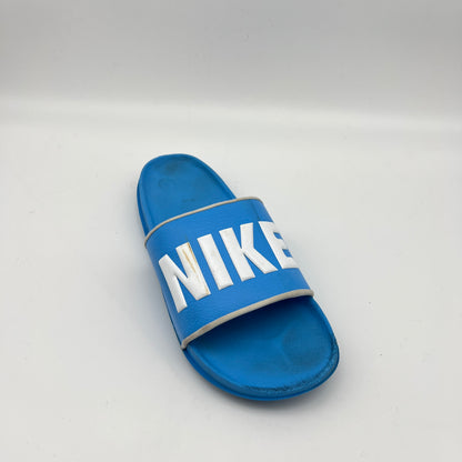 Side view of a bright blue Nike Benassi JDI slide featuring a wide blue strap with a bold white Nike logo and a contoured, textured comfort footbed.