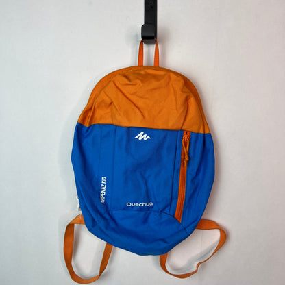 Blue and orange Quechua Arpenaz Kid 7 liter hiking backpack for children hanging on a white wall.
