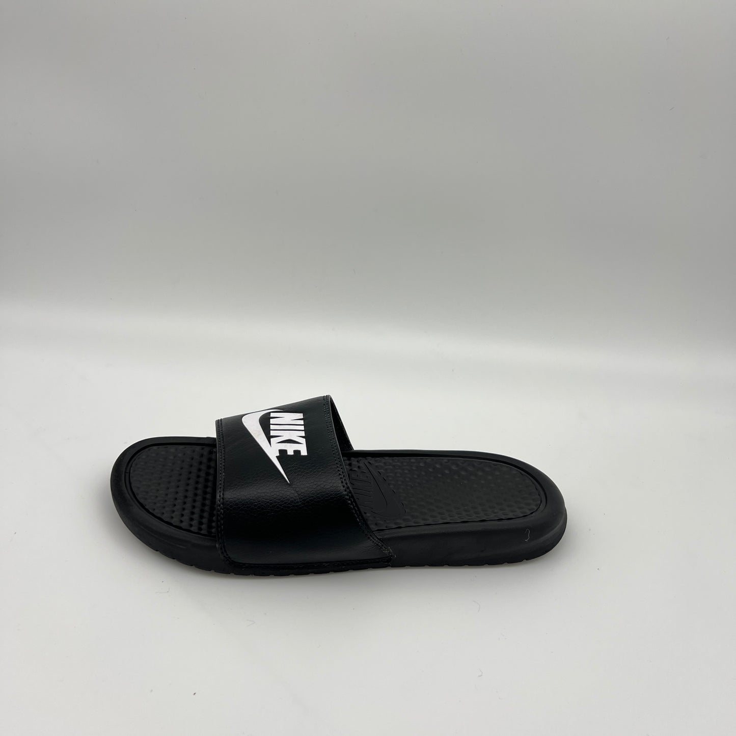 Side view of a single black Nike Benassi JDI slide sandal featuring a bold white Swoosh logo on the strap and a textured footbed on a plain white background.