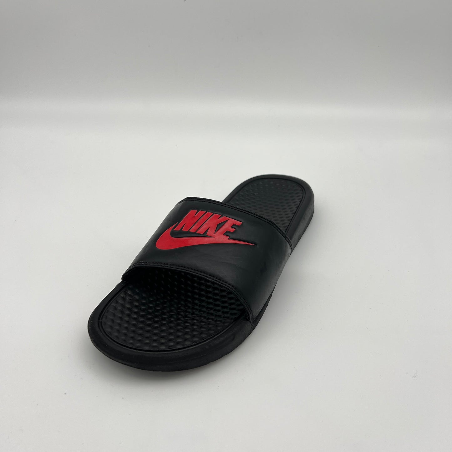 Side view of black Nike Benassi JDI slides featuring a padded synthetic leather strap and massage-textured footbed.