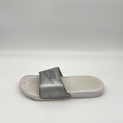 Metallic silver Nike Benassi JDI slide sandal with an embossed Nike logo on the strap and a textured white footbed, shown on a white background.