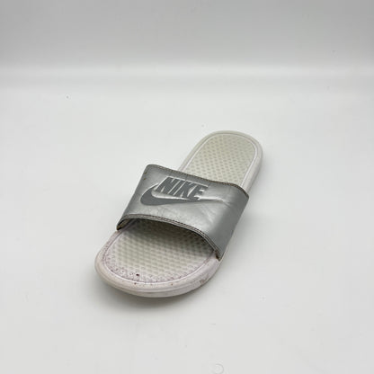 Metallic silver Nike Benassi JDI slide sandal with an embossed Nike logo on the strap and a textured white footbed, shown on a white background.