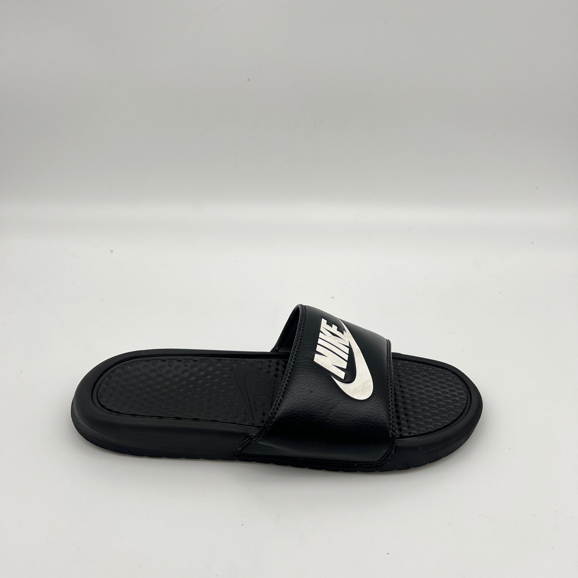 Side view of Nike Benassi JDI slide sandal in black and white with a textured footbed