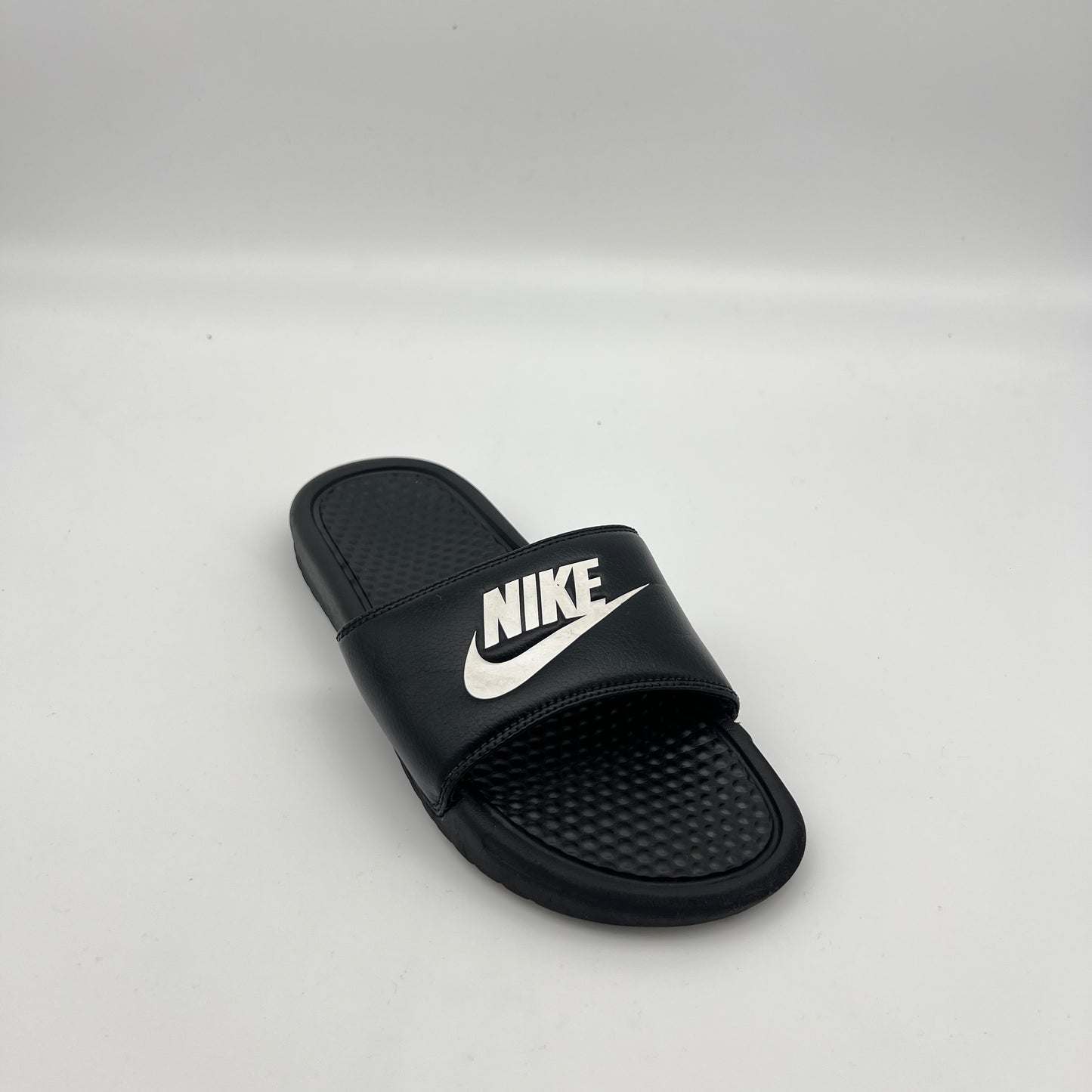 Nike athletic slides featuring a black synthetic strap with a white logo and cushioned sole