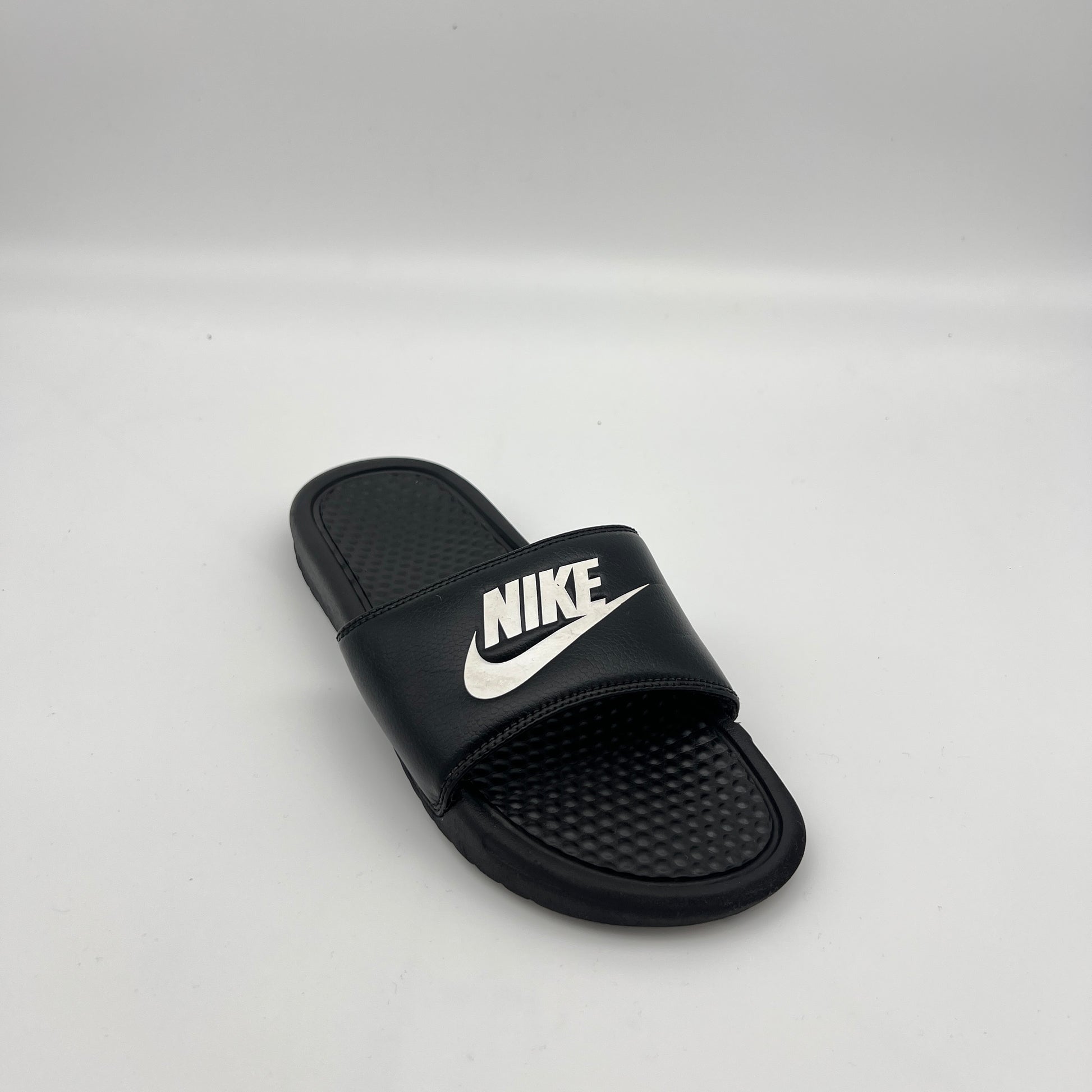 Nike athletic slides featuring a black synthetic strap with a white logo and cushioned sole