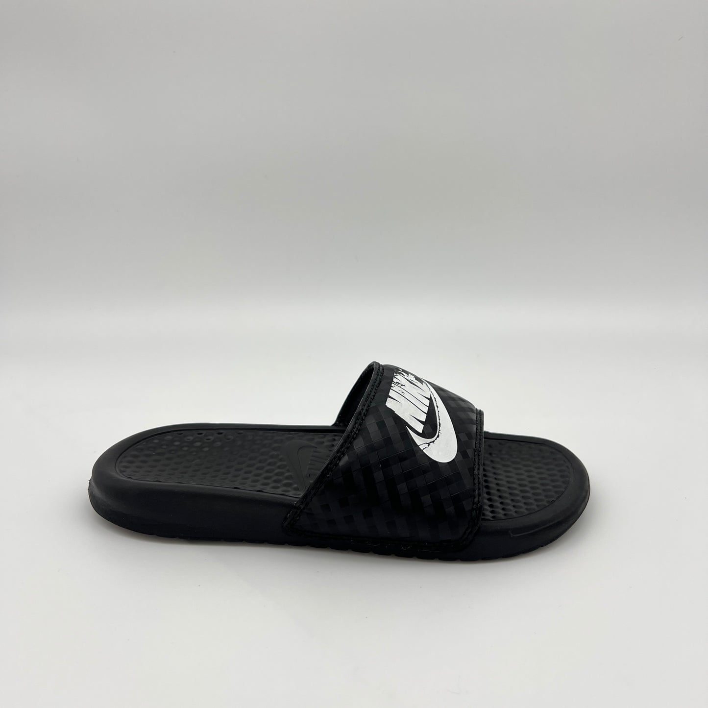 Side profile of black Nike Benassi JDI women's slides with a white Nike logo and diamond-patterned strap