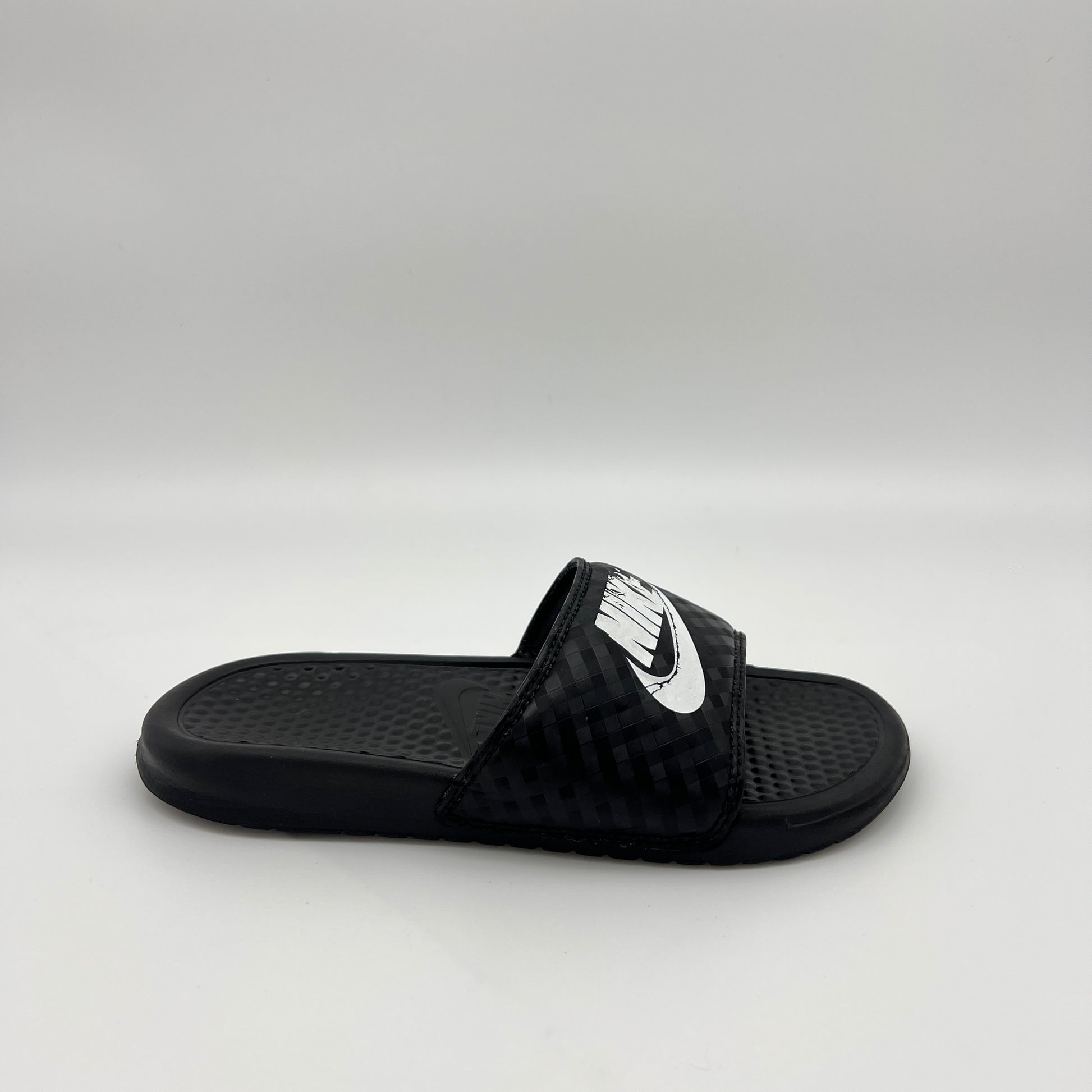 Side profile of black Nike Benassi JDI women's slides with a white Nike logo and diamond-patterned strap