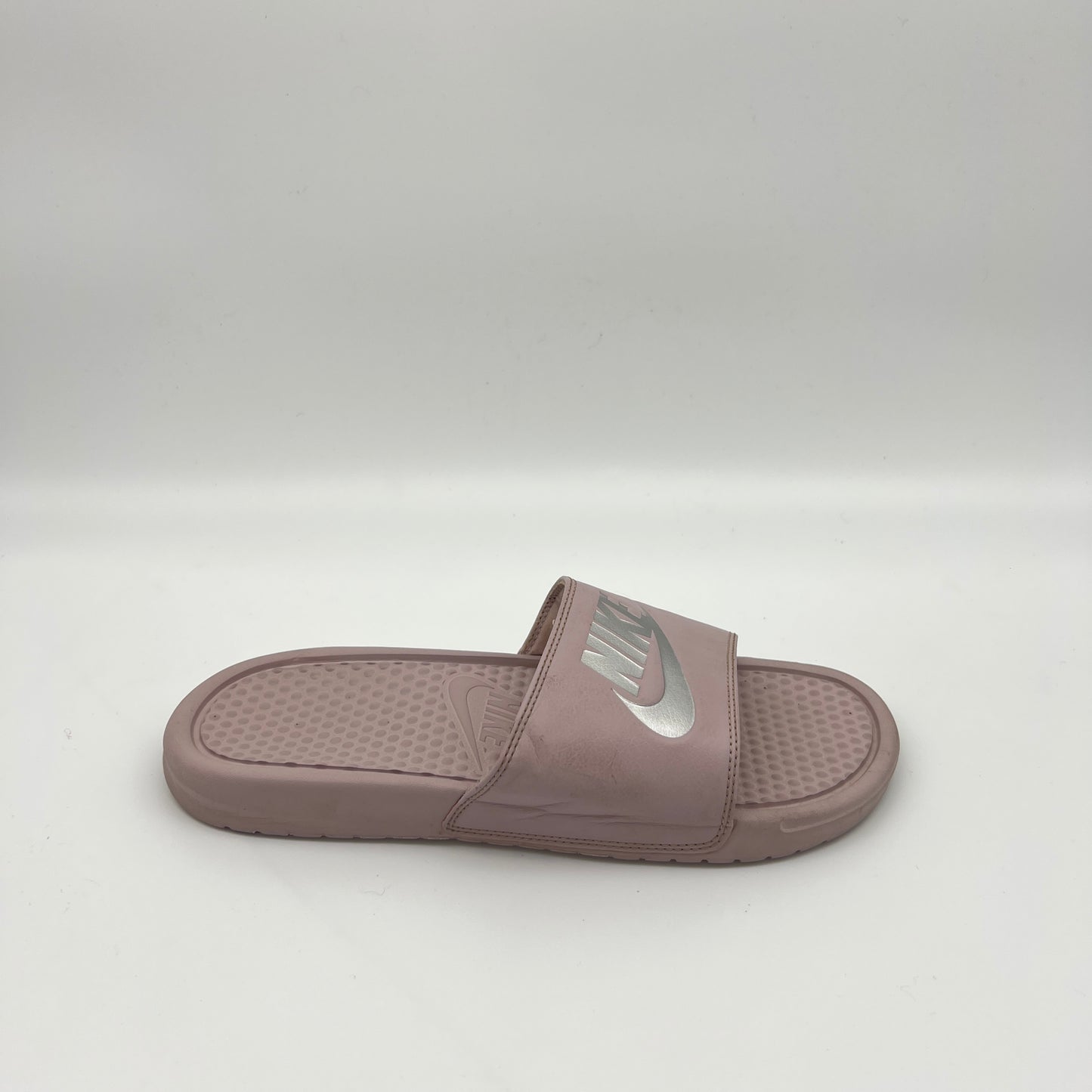 Side view of a mauve Nike Benassi JDI slide sandal featuring a metallic silver Nike logo on the strap and a textured Solarsoft foam footbed.