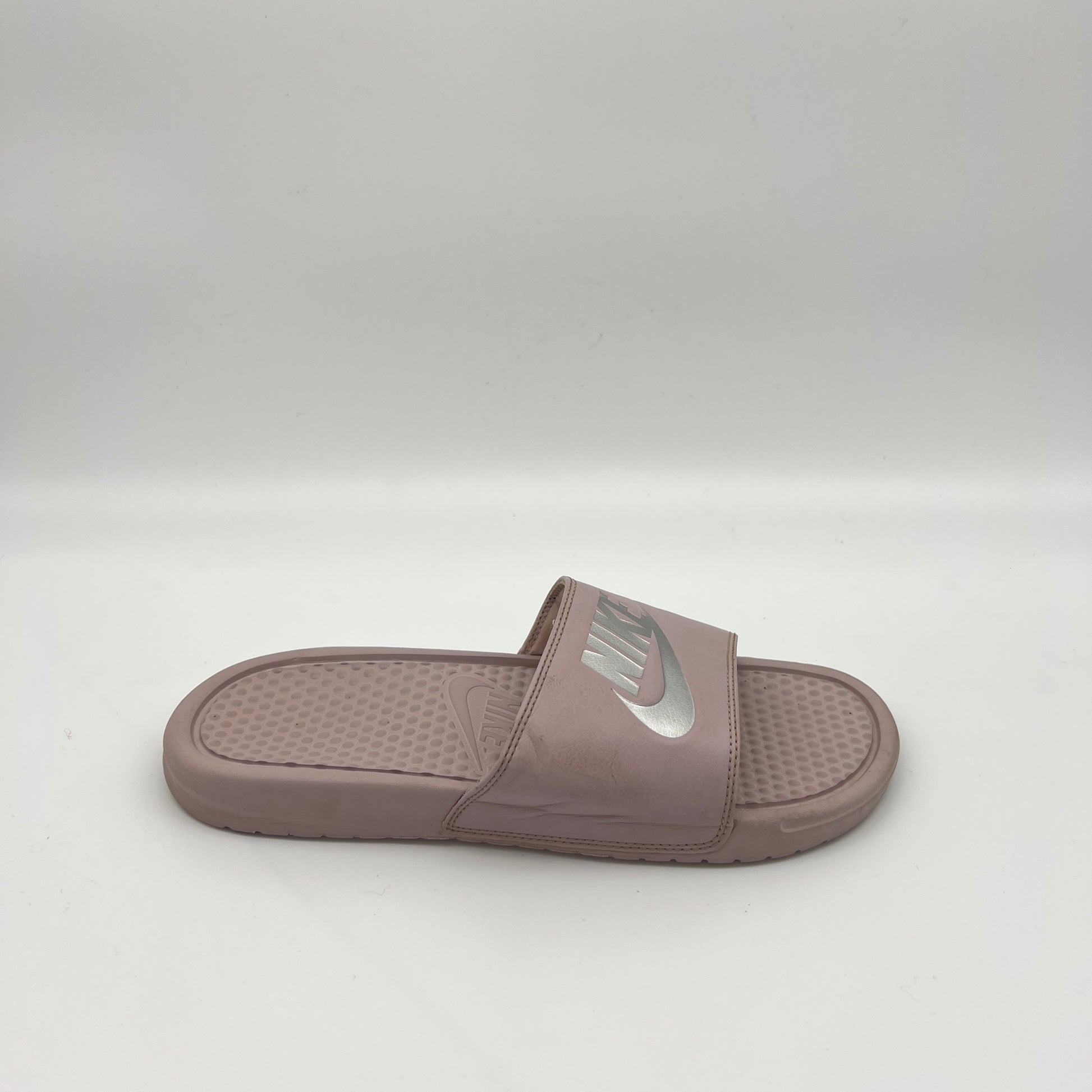 Side view of a mauve Nike Benassi JDI slide sandal featuring a metallic silver Nike logo on the strap and a textured Solarsoft foam footbed.