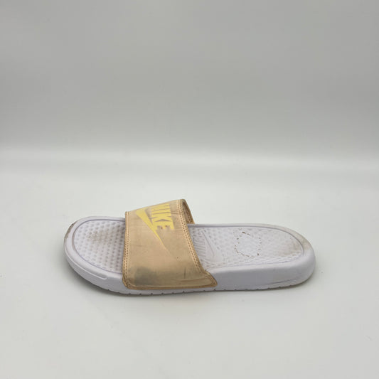 Side view of a pale ivory Nike Benassi JDI slide featuring a yellow Nike logo on the padded strap and a textured white Phylon footbed on a white background.