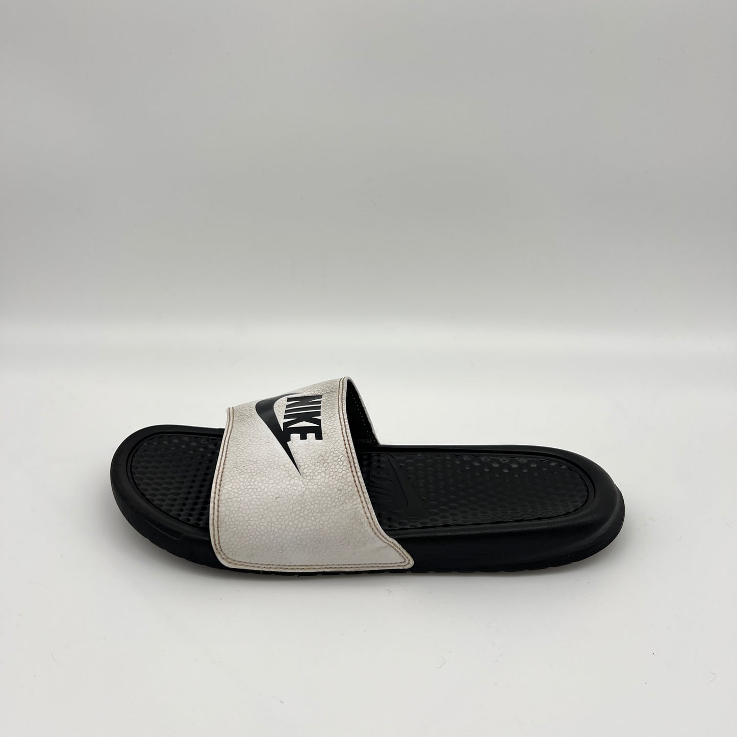 Side view of a Nike Benassi JDI slide with a white pebbled-texture strap and black Nike logo, featuring a textured black footbed on a clean white background.