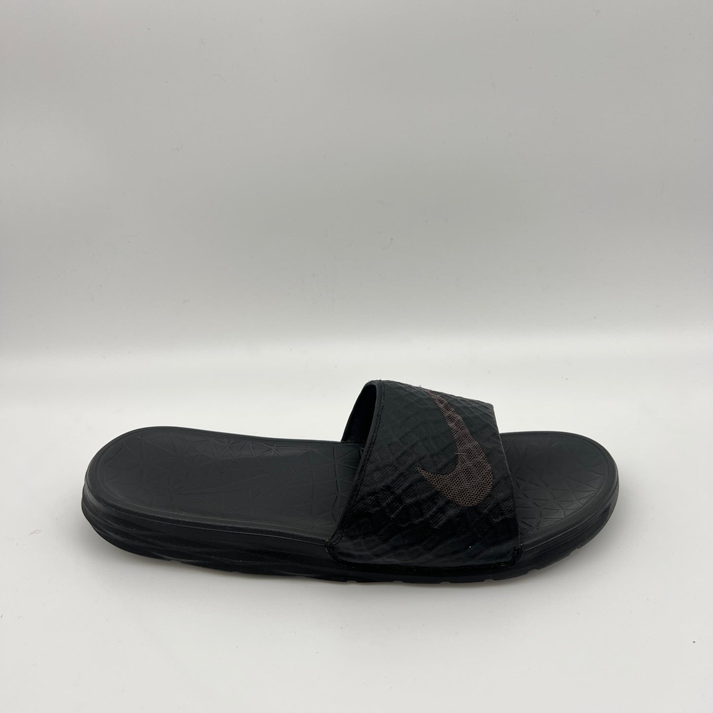 Side view of a triple black Nike Benassi Solarsoft slide with a geometric-patterned strap, a subtle dark swoosh logo, and a textured comfort footbed.