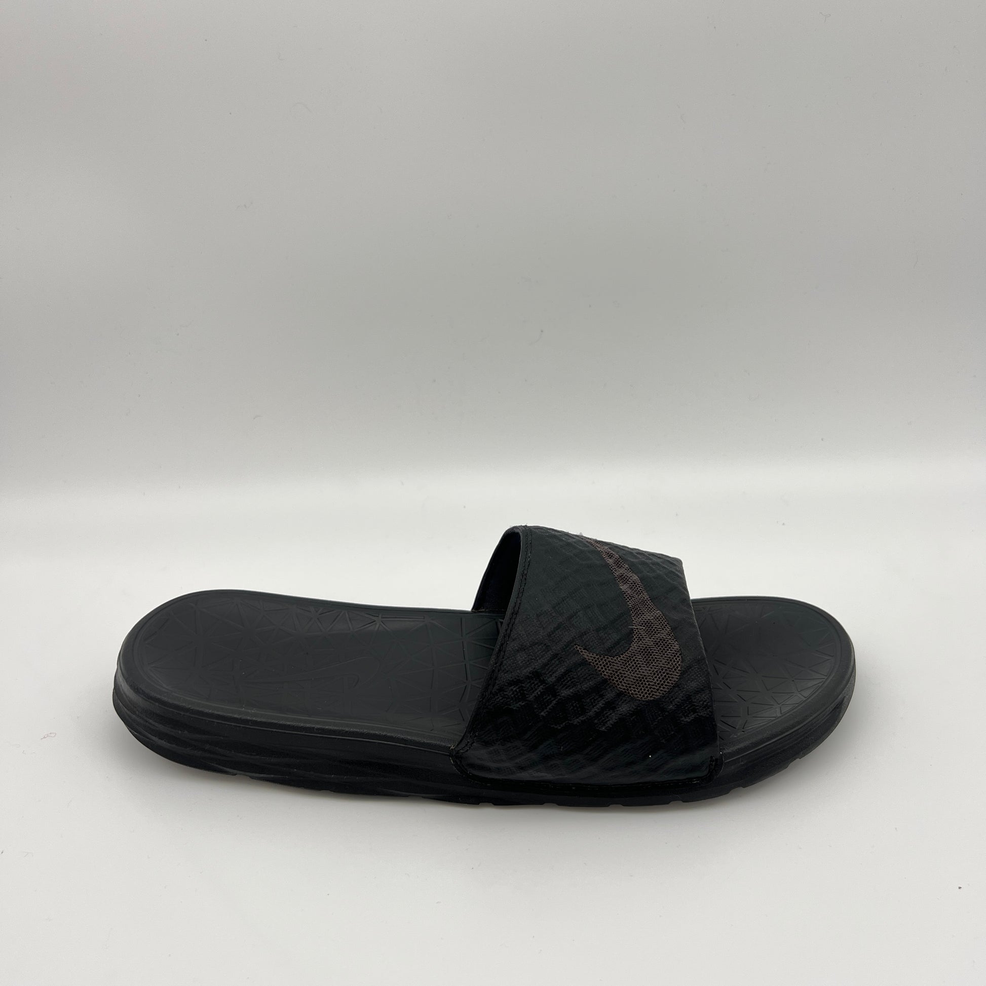 Side view of a triple black Nike Benassi Solarsoft slide with a geometric-patterned strap, a subtle dark swoosh logo, and a textured comfort footbed.