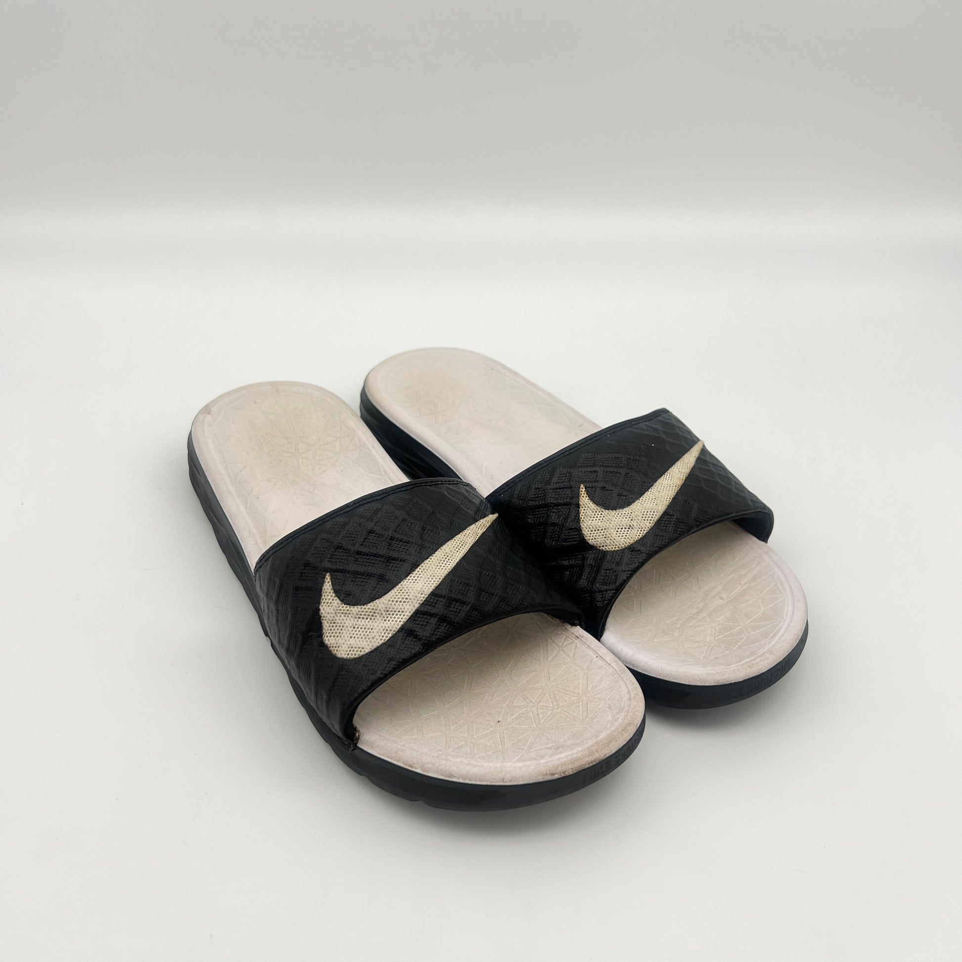 Black and beige Nike slides on a light gray background